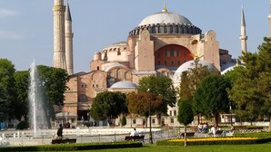 A historic building with a large dome and minarets, surrounded by a well-maintained garden with a fountain.