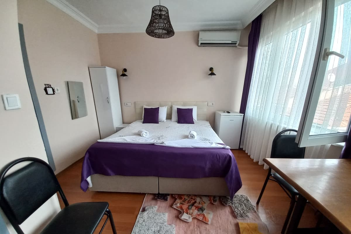 A hotel room with a bed, a desk, a chair, an air conditioner, and a window with curtains.
