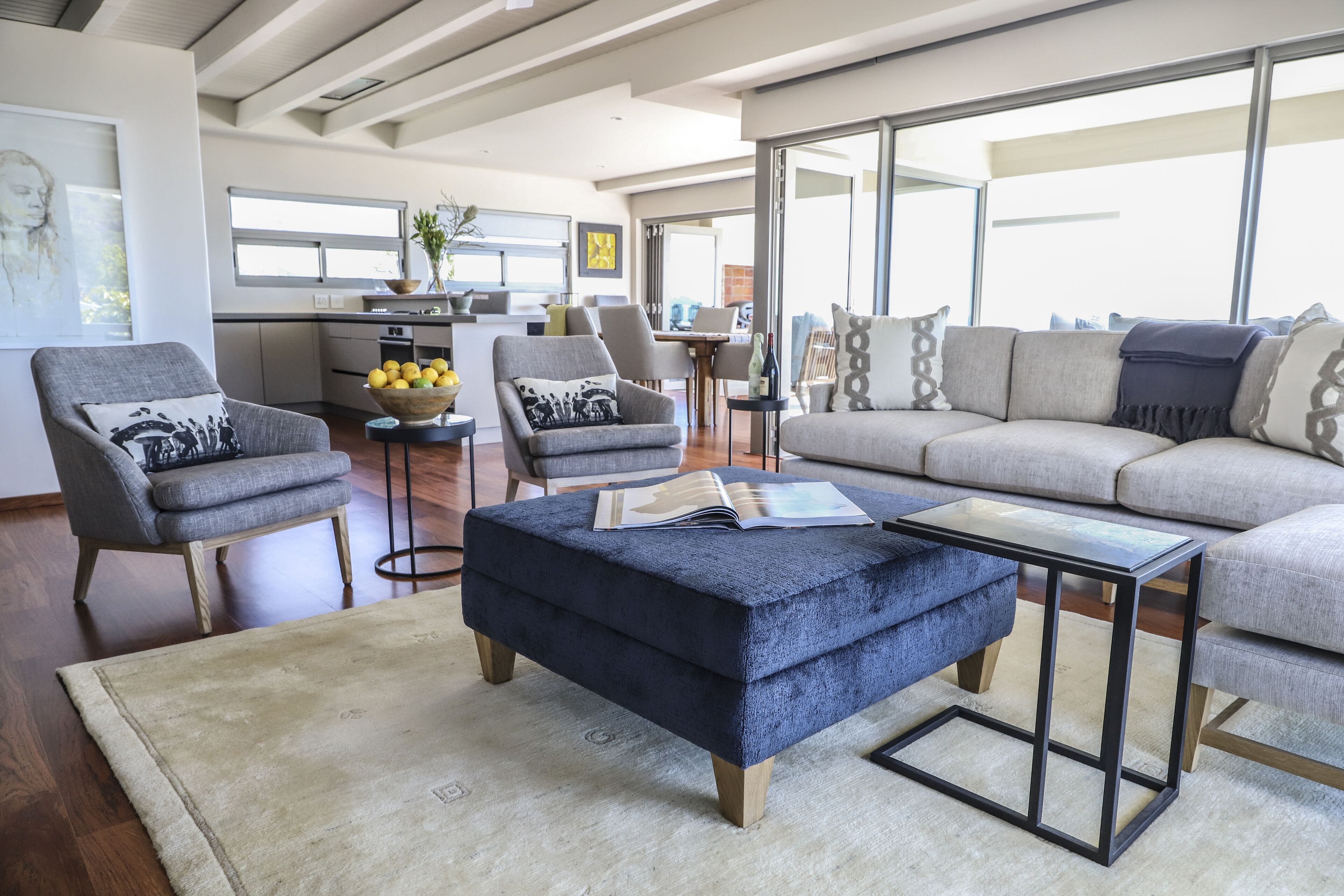 A modern living room with a sofa, armchairs, a coffee table, and a dining area in the background.