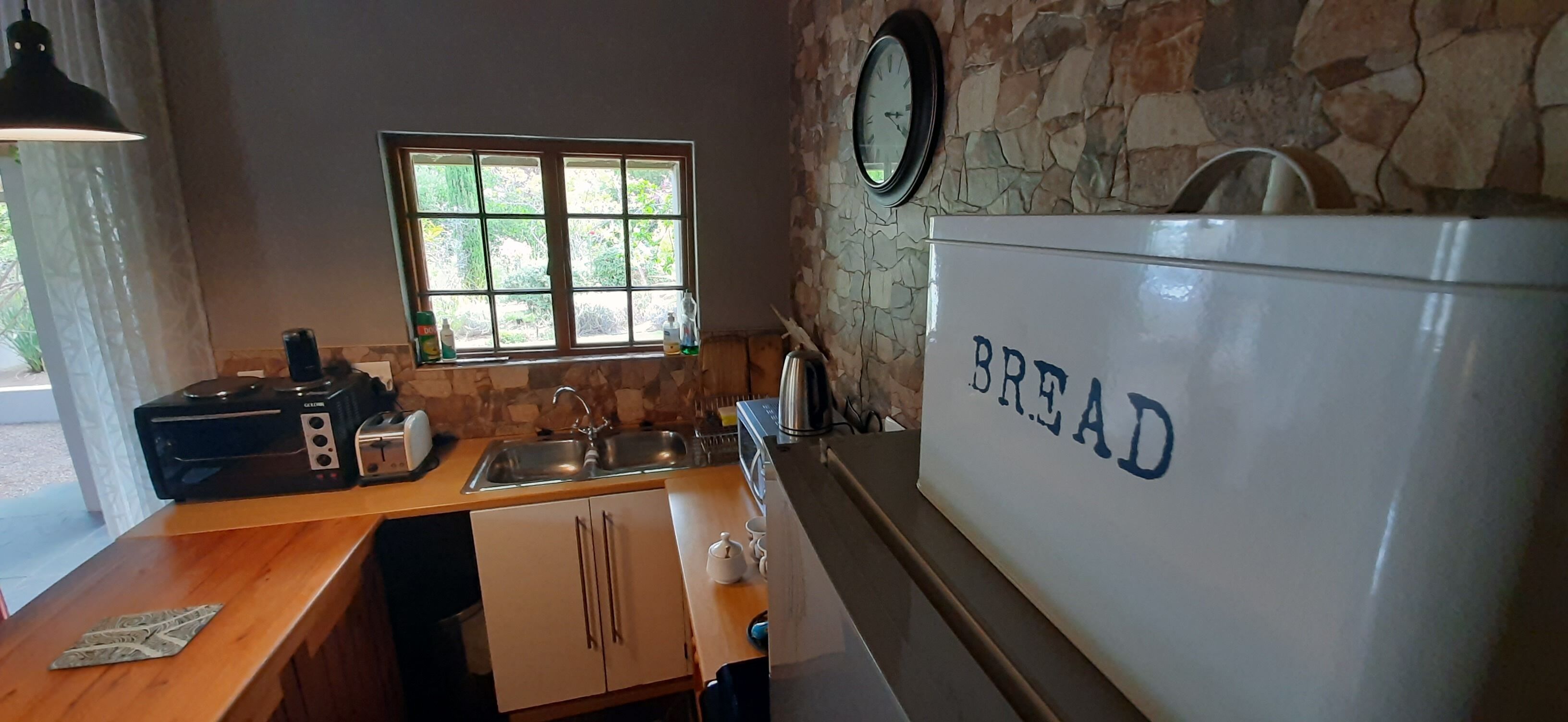Una cocina con pared de piedra, una ventana, refrigerador para pan y un reloj.