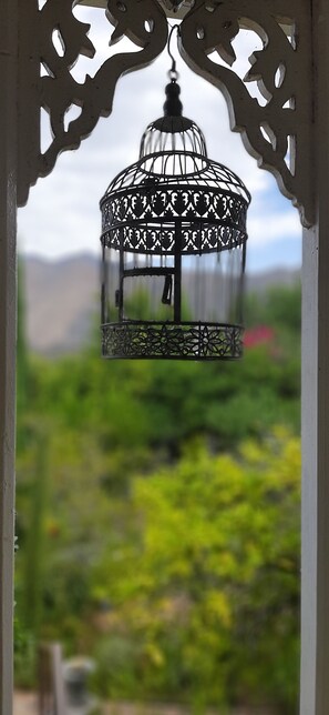 A metal birdcage lantern hanging from an ornate structure with a blurred green landscape in the background. - Abigails Garden Cottage (Montagu)