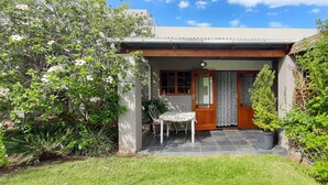 A small house with a covered porch, a table and chair, and a potted plant. - Abigails Garden Cottage (Montagu)