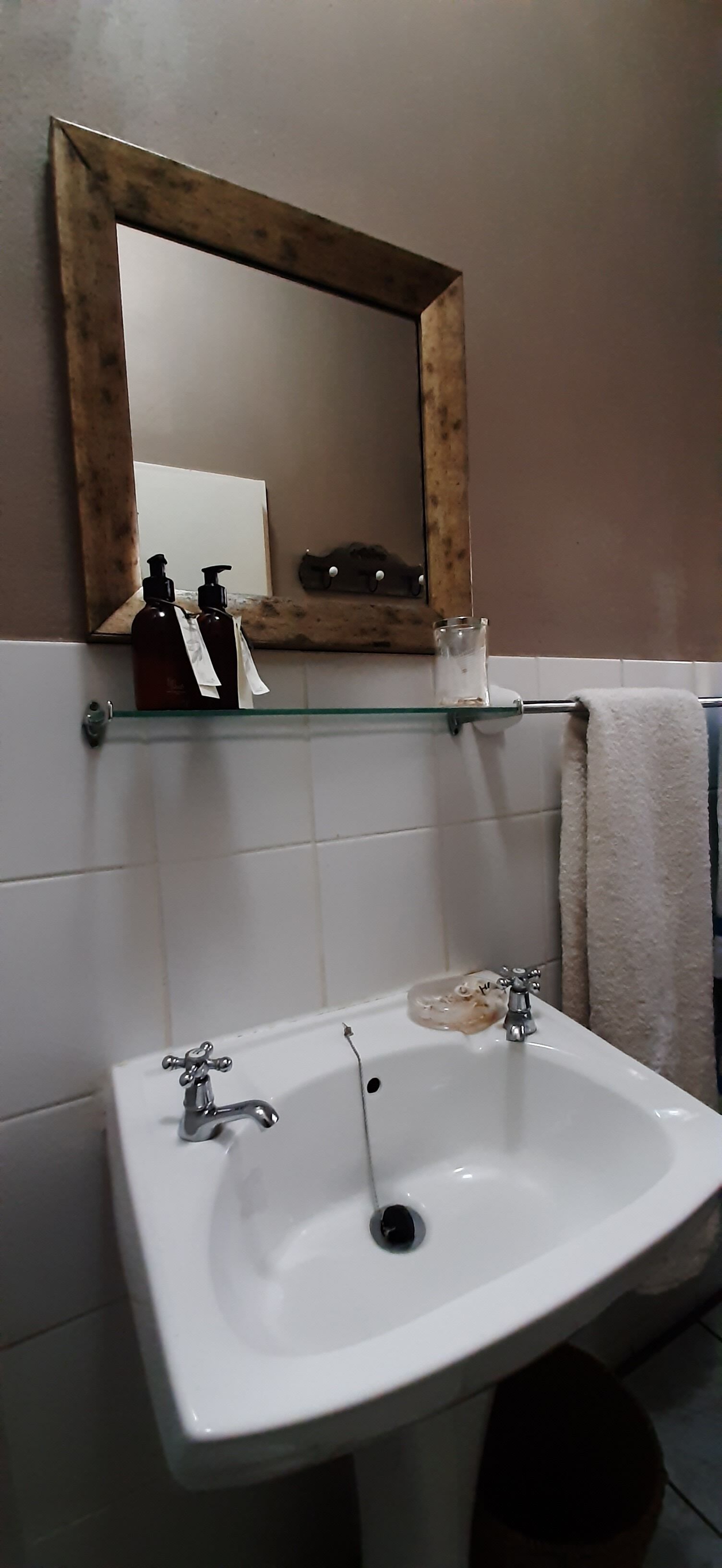 A bathroom with a white sink, a wooden-framed mirror, and a glass shelf above the sink.