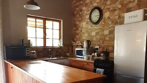 A kitchen with a wooden island, stone wall, and a clock. - Abigails Garden Cottage (Montagu)