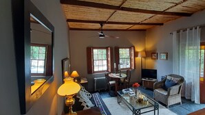 A cozy living room with a wooden ceiling, a sofa, a coffee table, and a TV. There are two windows with curtains, a lamp, and a radiator. - Abigails Garden Cottage (Montagu)