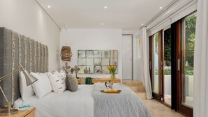 A modern bedroom with a large bed, a bedside table, a lamp, and a view of the outdoors through a sliding glass door. - Le Thallo (Cape Town)