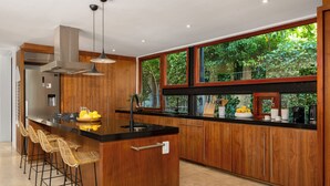 A modern kitchen with a central island, bar stools, a stainless steel refrigerator, and a large window with a view of greenery. - Le Thallo (Cape Town)