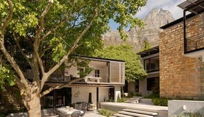 Una casa moderna con techo plano, un gran árbol en primer plano y una montaña al fondo.