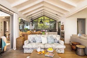 A spacious living room with a high ceiling, a sofa set, a coffee table, and a kitchen in the background.