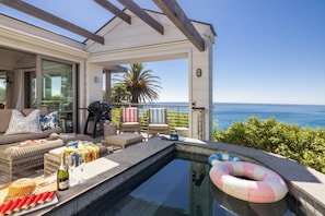 A pool area with a view of the ocean, outdoor seating, and a pergola.
