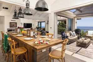 A spacious kitchen with a wooden island, dining chairs, and hanging metal pendant lights. - Bungalow Ulusaba (Cape Town)