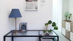 A modern living room with a glass coffee table, a blue lamp, a framed abstract painting, a potted plant, and a telephone on the wall. - B&B Civico 13 (Naples)