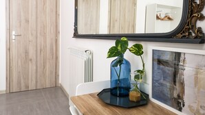A room with a wooden door, a radiator, a blue vase with a plant, a wooden table, and a large mirror. - B&B Civico 13 (Naples)