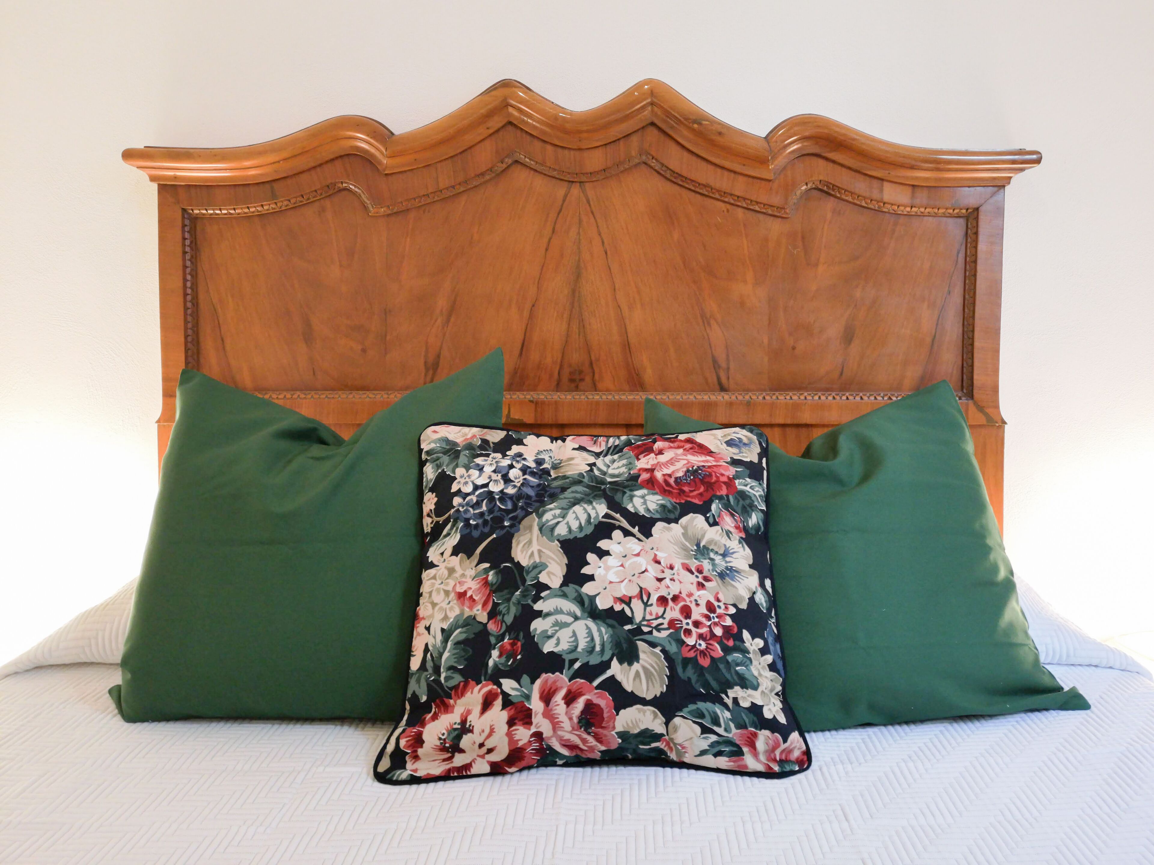 Ein Bett mit einem Holz-Kopfteil, zwei grünen Kissen und einem blumigen Kissen.