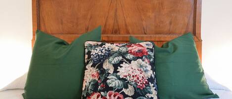 Ein Bett mit einem Holz-Kopfteil, zwei grünen Kissen und einem blumigen Kissen.