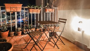 A balcony with a wooden table and chairs, potted plants, and a view of the city at night. - B&B Civico 13 (Naples)