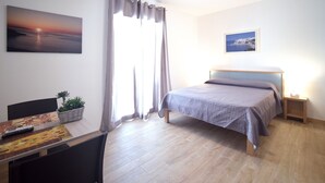 A bedroom with a bed, a desk with a plant, a painting, and a nightstand with a lamp. - Residenza Montegrappa (Peschici)