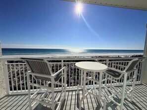 Un balcon avec des balustrades blanches, deux fauteuils en osier et une petite table ronde.