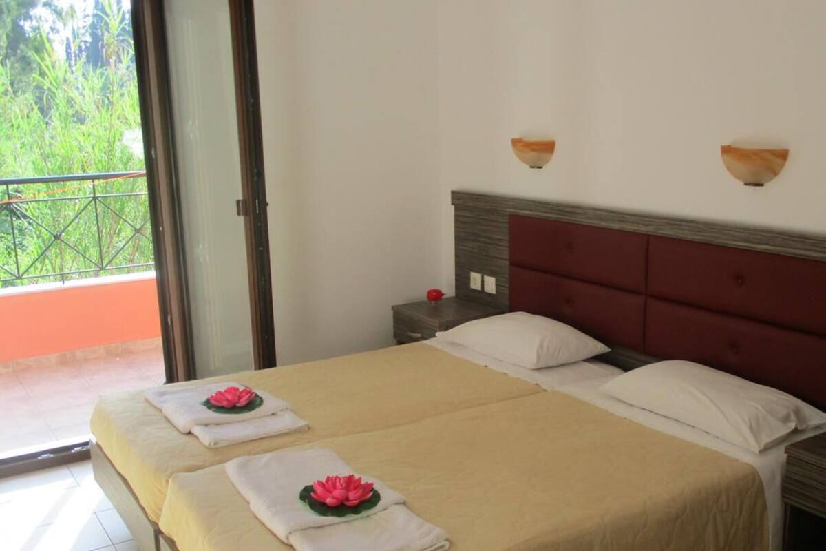 Un lit double avec une couvre-lit beige et deux oreillers, une tête de lit rouge et deux appliques murales.