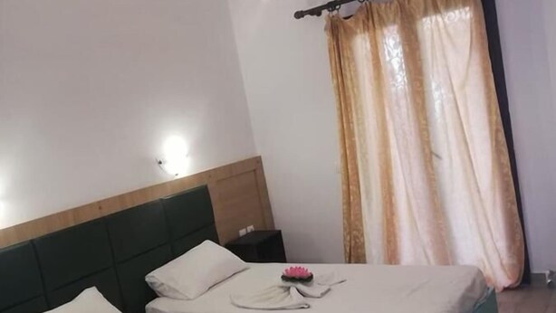 A hotel room with two beds, each with a pillow and a folded towel. There is a ceiling light fixture and an air conditioning unit on the wall.
