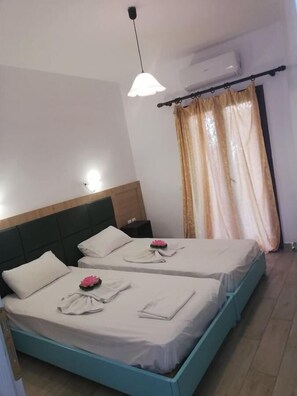 Een hotelkamer met twee bedden, elk met een kussen en een opgevouwen handdoek. Er is een plafondlamp en een airconditioner aan de muur.