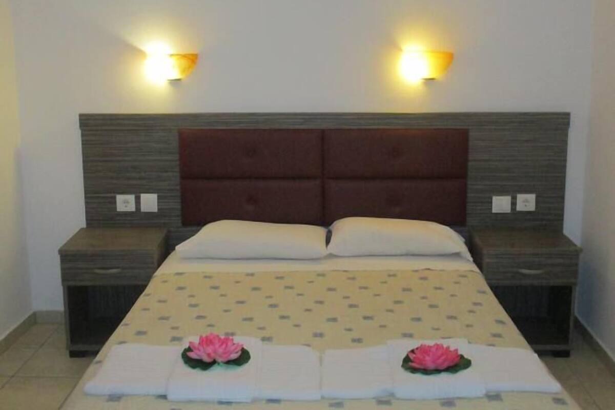Une chambre d’hôtel avec un lit double, deux tables de chevet et deux lampes fixées au mur.