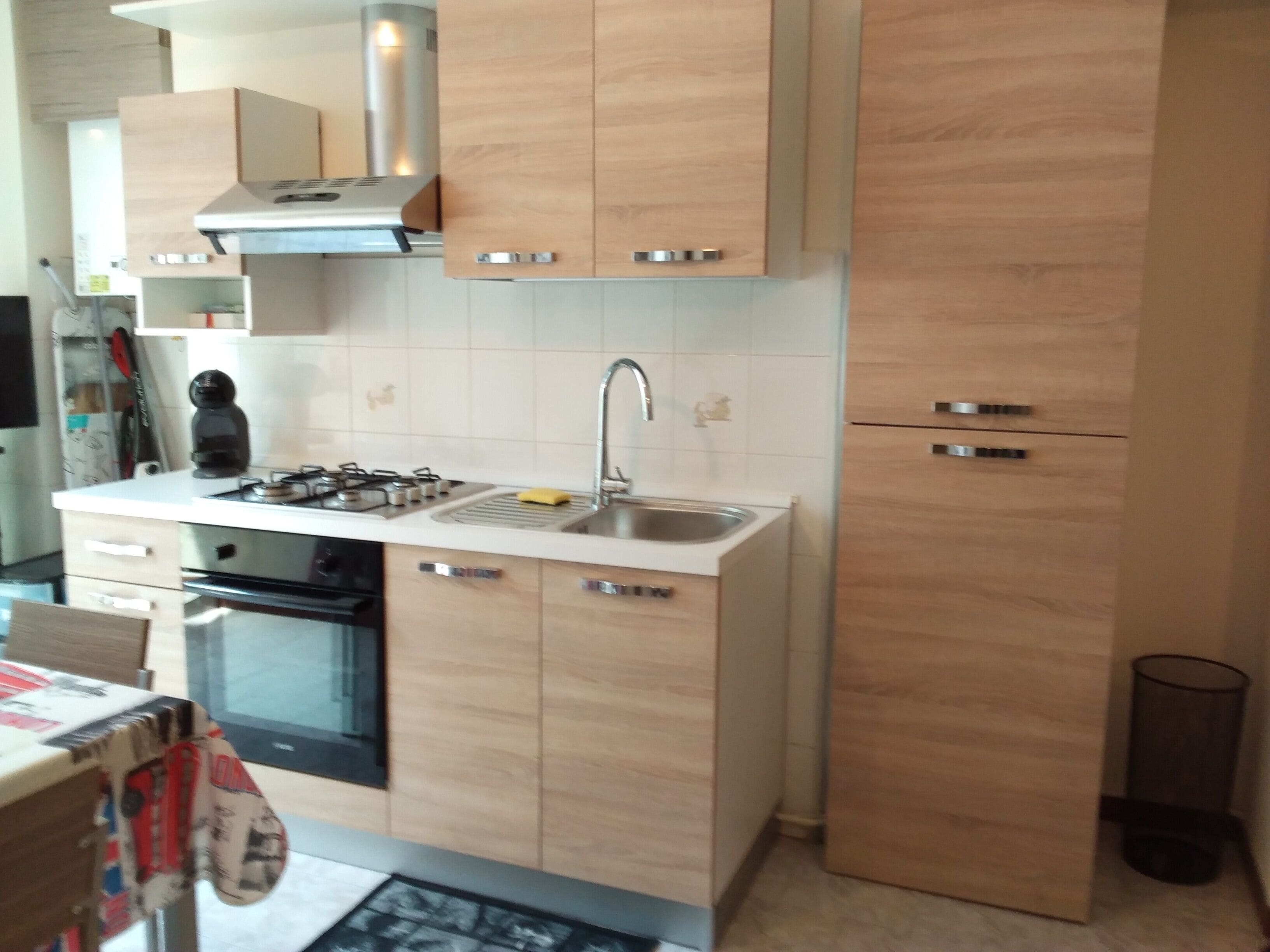 A modern kitchen with light wood cabinets, stainless steel appliances, and a built-in oven.