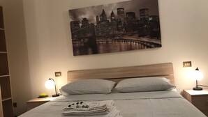 A neatly made bed with folded towels and a cityscape painting above it. - Kibilù - Viale Bligny OSV (Milan)