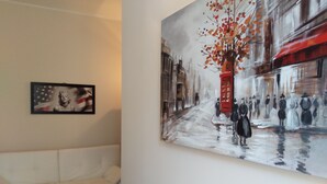 A room with a large painting of a street scene, a white sofa, and a table with various items. - Kibilù - Viale Bligny OSV (Milan)