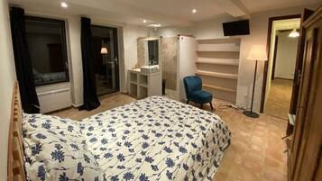 Une chambre à coucher comprenant un lit, une chaise, un téléviseur, un miroir, ainsi qu’une salle de bain avec une douche et un lavabo.