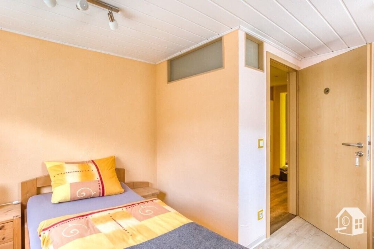 Ein Schlafzimmer mit Bett, Nachttisch und einer Tür zu einem weiteren Raum.
