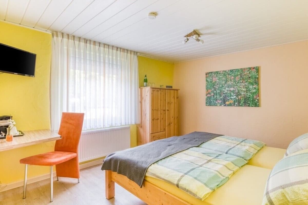 Ein Schlafzimmer mit Bett, Schreibtisch, Stuhl, Fernseher und einem Fenster mit Vorhängen.
