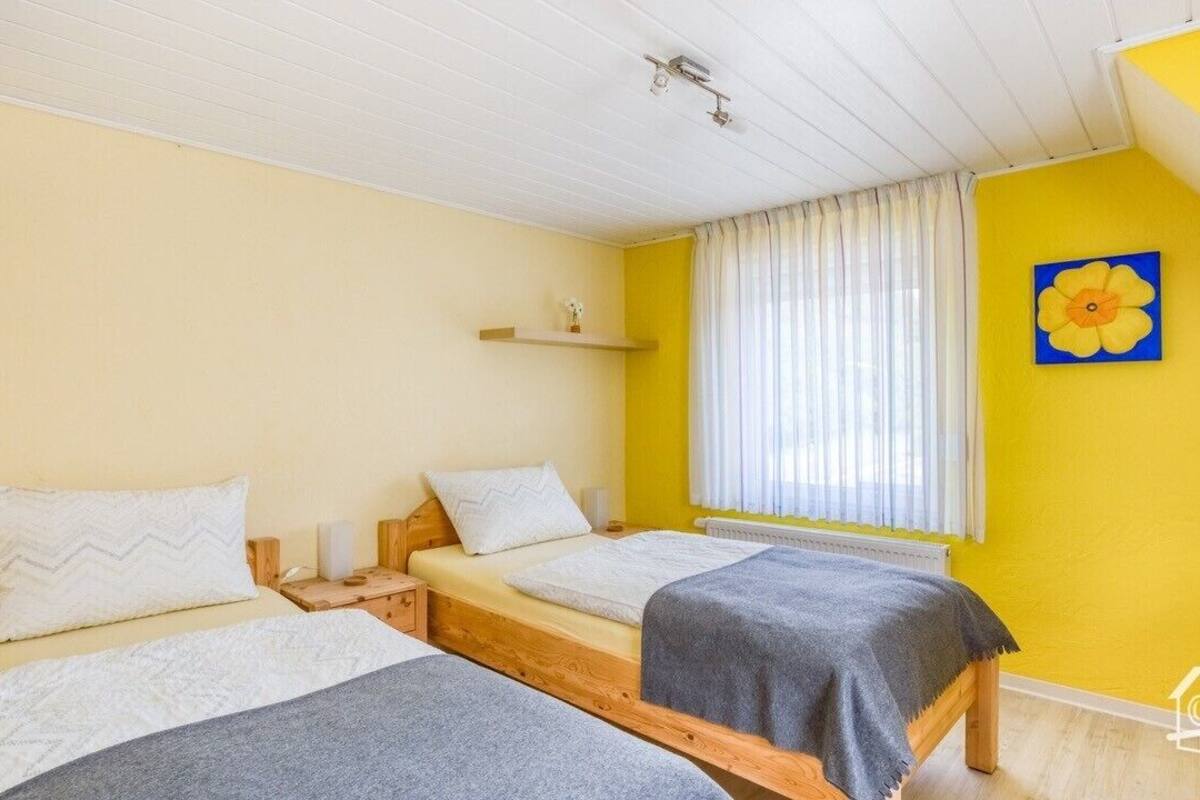Ein Zimmer mit zwei Betten, einem fensterbepften Fenster, einem Regal mit einer Vase und einem Gemälde an der Wand.