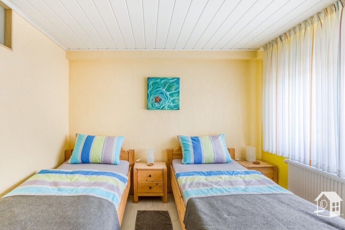 Ein Zimmer mit zwei Betten, jeweils mit gestreifter Bettwäsche, einem kleinen Nachttisch und einem an der Wand hängenden Kunstwerk.