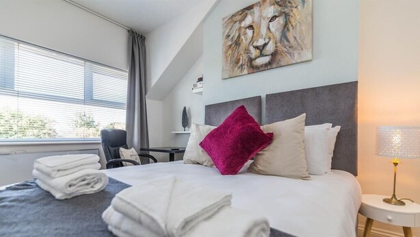 A hotel room with a bed, a desk, a chair, and a window with blinds. - West Bridgford Classy 2bed Flat (Nottingham)