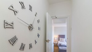 A hallway with a large wall clock and a door leading to a bedroom with a bed and a bedside table. - West Bridgford Classy 2bed Flat (Nottingham)