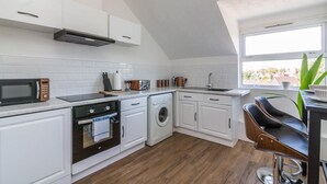 A compact kitchen with white cabinetry, a microwave, a toaster, a washing machine, and a sink. - West Bridgford Classy 2bed Flat (Nottingham)