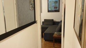 Un pasillo estrecho con un sofá gris y una mesita con un cuenco.