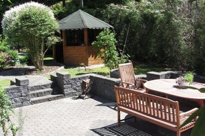 A patio area with a wooden gazebo, stone steps, and a round wooden table with chairs.