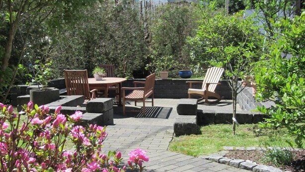 Un patio exterior con una mesa y sillas, rodeado de macetas de piedra y un pequeño árbol.