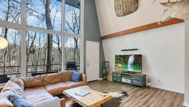 A modern living room with a leather sofa, a wooden coffee table, and a television. - The Reed – A Cozy Cabin in the Woods (Rockbridge)