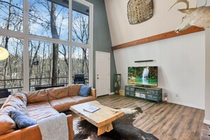 A modern living room with a leather sofa, a wooden coffee table, and a television. - The Reed – A Cozy Cabin in the Woods (Rockbridge)
