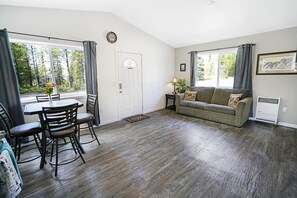 A room with a dining table, chairs, a sofa, and a window with curtains.
