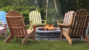 Un brasero rodeado de sillas Adirondack de distintos colores.