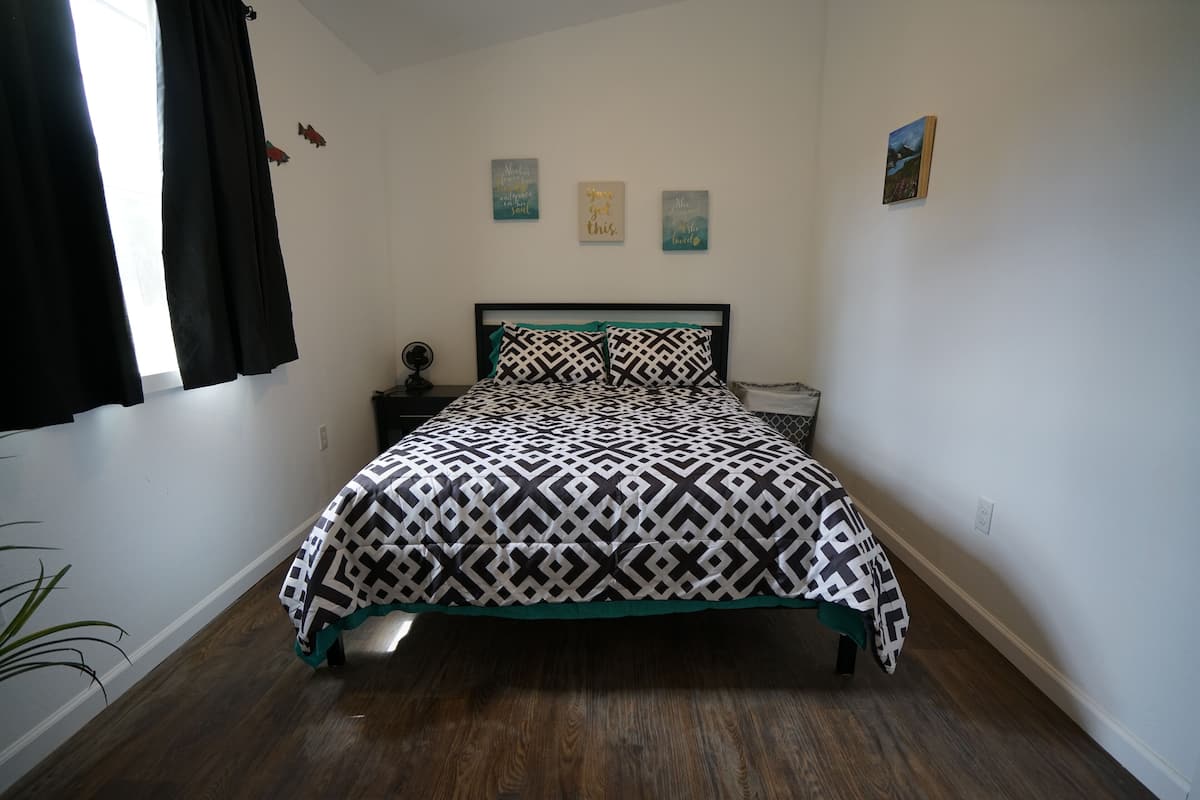 A bedroom with a bed, a bedside table, a wall clock, and three wall decorations.