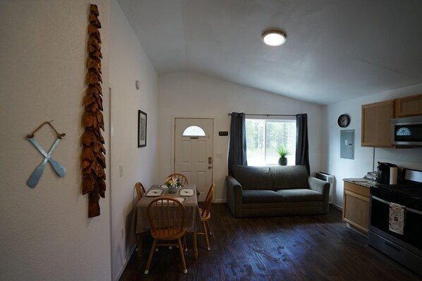A compact living space with a dining area, a sofa, a kitchen, and a window with curtains.