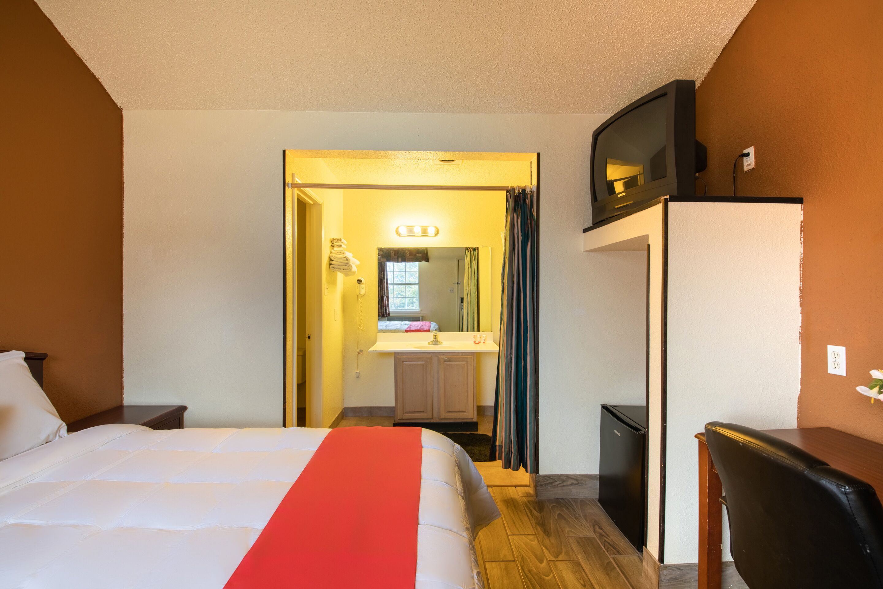 A hotel room with a bed, a desk, a television, and a refrigerator.