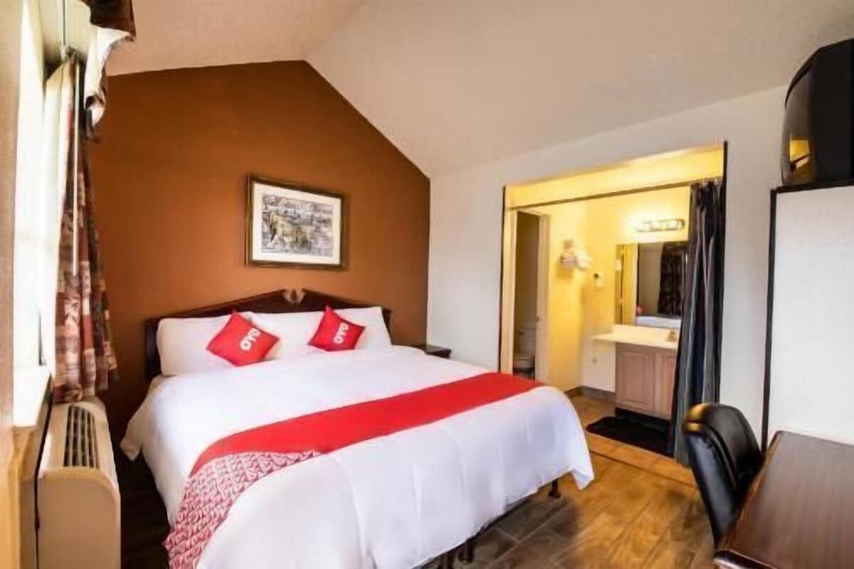 A hotel room with a bed, a framed picture on the wall, a door leading to a bathroom, and a chair.