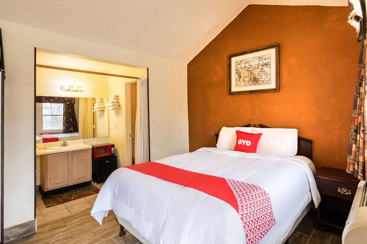A hotel room with a bed, a bathroom with a sink and mirror, a framed picture on the wall, and a red pillow with 'OYO' on it.