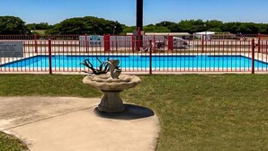 A swimming pool surrounded by a red fence, with a concrete pathway leading to a decorative stone structure. - OYO Hotel Decatur TX Hwy 287 Northwest (Decatur)